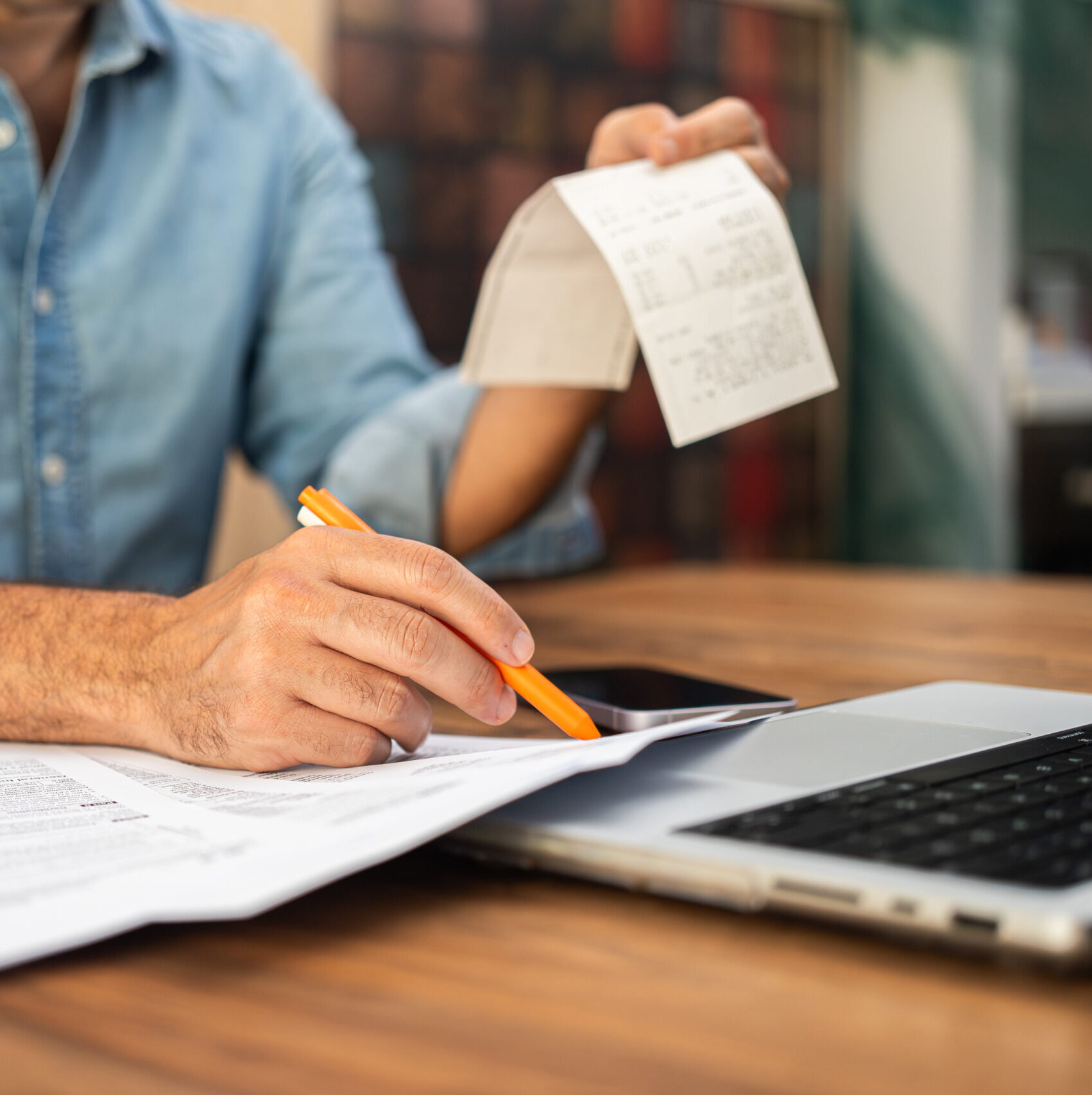 Man filling out tax forms at home using a laptop and holding receipts. Financial management and personal accounting concept during tax season